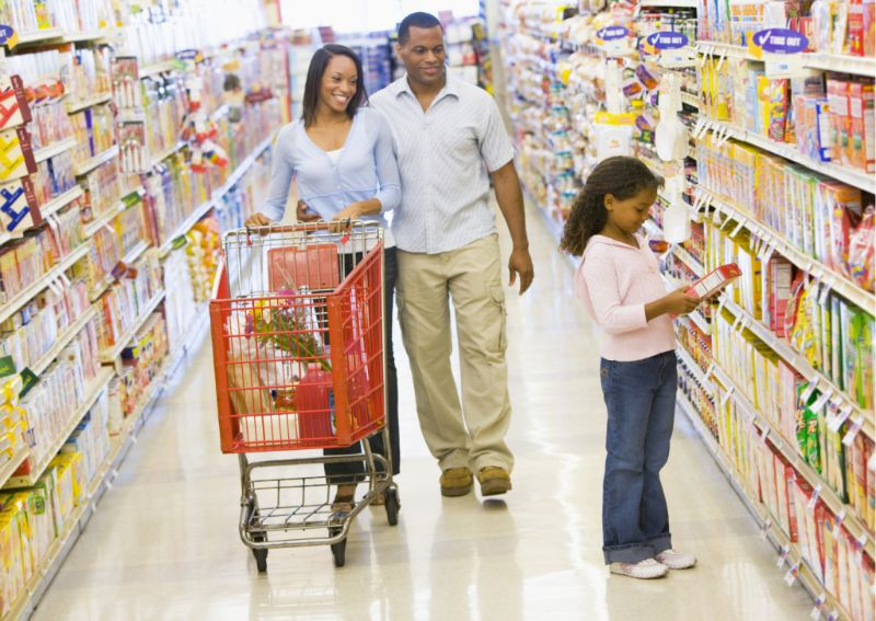 A family shopping at a grocery store with a full cart, learning how to save money on groceries